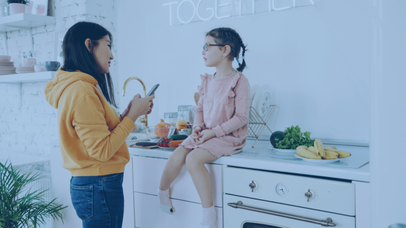 Image of mother reading message from teacher via cell phone to her child
